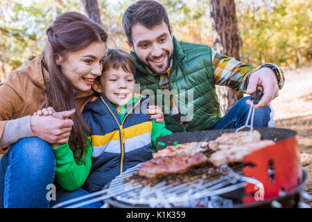 Close-up portrait of happy family grilling meat on barbecue grill in autumn park Stock Photo