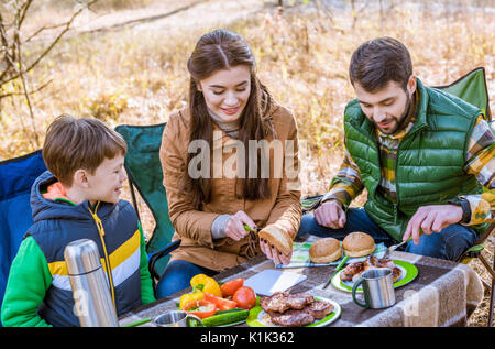 Happy smiling family eating and having fun while sitting at table on picnic in autumn forest Stock Photo
