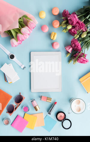 top view of tablet, various accessories, macarons and bouquets of flowers isolated on blue Stock Photo