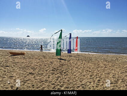 Fun with flags at Beach Fun hire in Palm Cove with the morning sun glistening on the water off the beautiful main beach stretch of sand Stock Photo