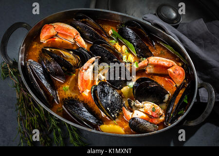 Seafood mussels crabs soup in metal pot, gray background Stock Photo