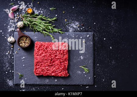 Raw fresh marbled mince meat and seasonings on dark background. Copy space, high angle view. Stock Photo