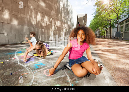 Beautiful curly girl and friends draw hopscotch game on the road Stock Photo