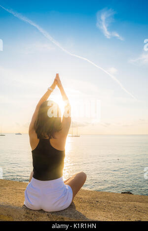 Young brunette woman (25-30) stretching while overlooking the sea in the Summer Stock Photo