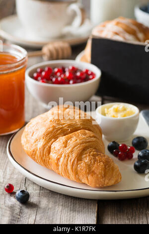 Continental breakfast with croissant, butter, jam, coffee and fruits. Closeup view, selective focus. Empty black chalkboard copy space for text Stock Photo