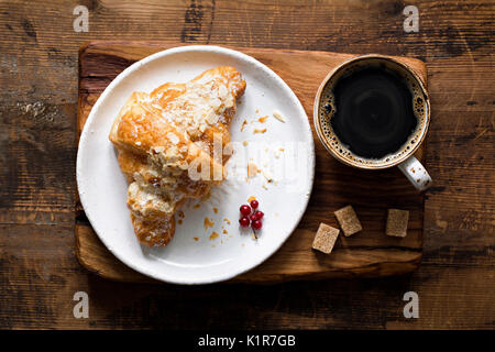 Almond croissant and cup of black coffee espresso on wooden cutting board. Table top view Stock Photo