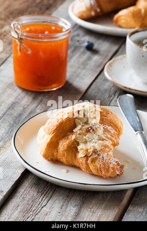 Continental breakfast croissant, jam in jar and cup of coffee on wooden table. Vertical, selective focus Stock Photo