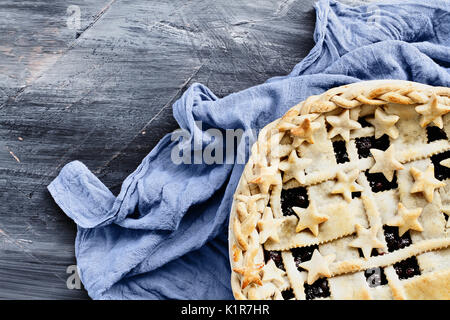 Top view of a blueberry pie with lattice and stars crust with grey napkin over an industrial artistic wooden background. Stock Photo