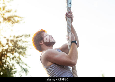 Climed higer and higher. Ginger sportsman doing exercise at rope. outdoor shot Stock Photo