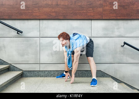 Young adult berded and redhead man looking forward and doing streaching. Outdoor Stock Photo