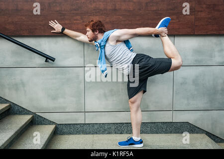 Fitness sport young adult redhead man in sportswear doing yoga fitness exercise in the city street over gray concrete background. Outdoor sports cloth Stock Photo