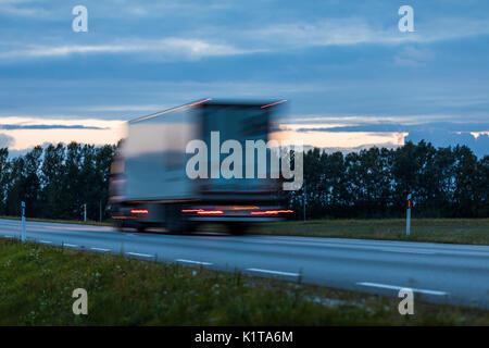 Speeding motion blur oncoming trucks with glowing lights on the highway after sunset. Abstract blur image background with copy space. Stock Photo