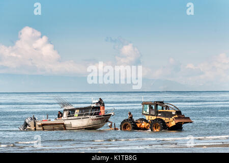 Fishing boats are towed by a tractor tug that will carry them back to land on the beach at Anchor Point, Alaska. The unique boat launch uses logging skidders to tow fishing boats from the Cook Inlet up the steep beach to the parking area and is the result of extreme tide that would make launching a boat impossible otherwise. Stock Photo