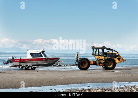 Fishing boats are towed by a tractor tug that will carry them back to land on the beach at Anchor Point, Alaska. The unique boat launch uses logging skidders to tow fishing boats from the Cook Inlet up the steep beach to the parking area and is the result of extreme tide that would make launching a boat impossible otherwise. Stock Photo