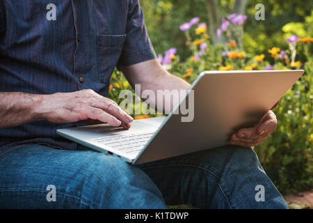 Cropped image of a mature man working on his laptop in garden, old male blogger typing on notebook Stock Photo