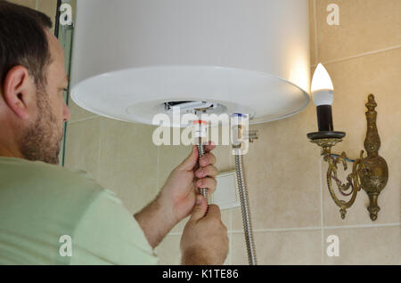 Man installing pipes for hot and cold water on a boiler in a bathroom Stock Photo