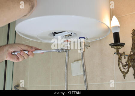 Man's hands with a wrench screwing pipes for hot and cold water on a boiler Stock Photo