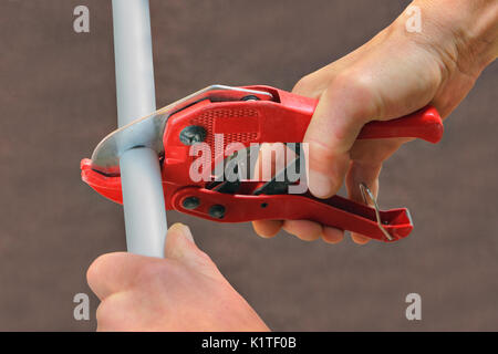 Using a cutter for plastic pipes when repairing domestic water pipes, hand plumbing close-up. Stock Photo