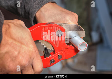 Close-up of a hand plumber using a cutter for plastic pipes. Stock Photo