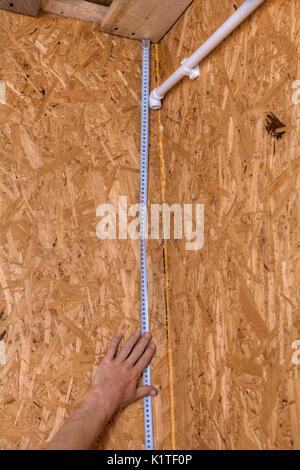 Plumber installing pipes in home, measurement of distance on a wooden wall using a measuring tape, wall mounting of a plastic water pipe. Stock Photo