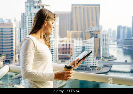 Mature woman is reading a book on her balcony in a highrise building Stock Photo