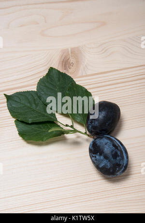 Two ripe plums with green leaves on a wooden background Stock Photo