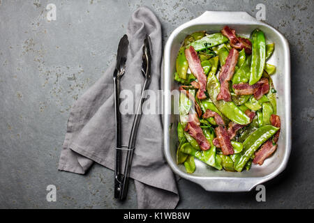Fried Peas pod with bacon in metal pot, slate background. Top view Stock Photo