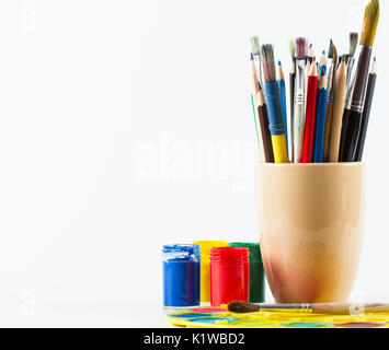 Paint brushes and pencils in mug and colorful paints on white background Stock Photo