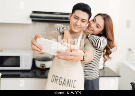 Happy asian couple smiling and cooking in the kitchen doing selfie using a smart phone Stock Photo