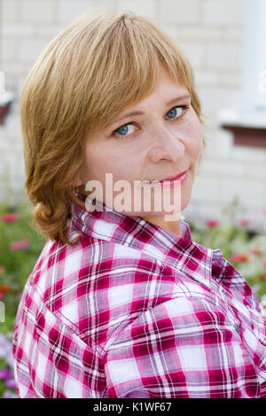 Happy woman with a flower relaxes in the grass with a flower. Woman looking at the camera. Middle-aged woman face close up. Stock Photo
