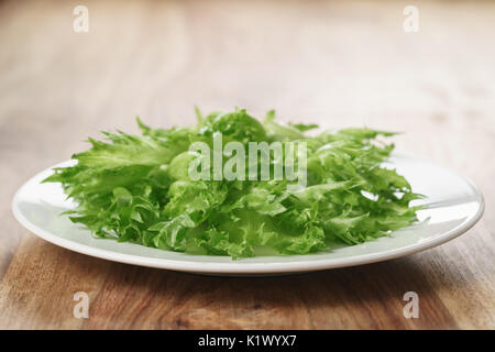 green frillice lettuce on white plate on wooden table, closeup photo Stock Photo