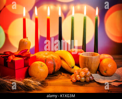 Kwanzaa festive concept with seven candles red, black and green, gift box, pumpkin, bowl and fruit on light blur bokeh background Stock Photo