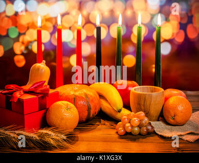 Kwanzaa holiday concept with decorate seven candles red, black and green, gift box, pumpkin, bowl and fruit on light blur bokeh background Stock Photo