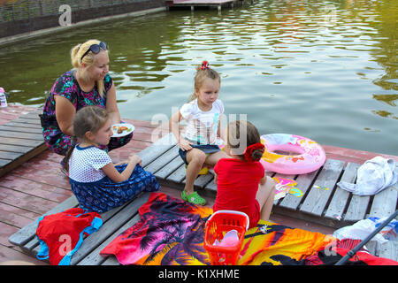 Three little girls play with toys on the wooden floor near the pond. August 2017 Stock Photo