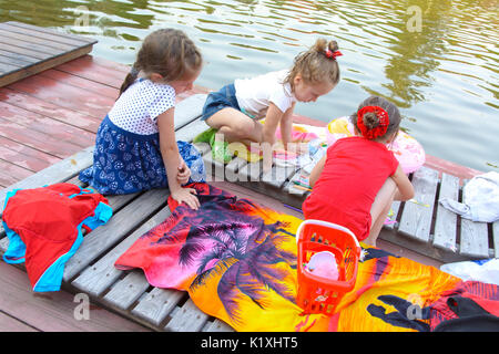 Three little girls play with toys on the wooden floor near the pond. August 2017 Stock Photo