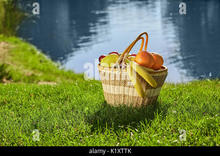 Picnic basket on green lawn. Fresh bananas and oranges. Benefits of eating healthy food. Stock Photo