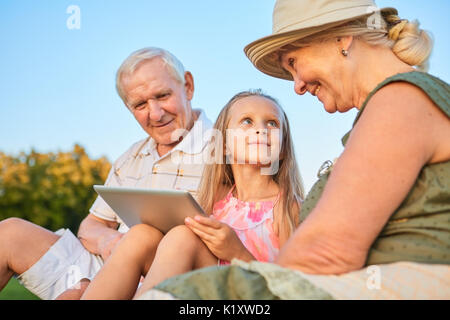 Child with a tablet, grandparents. Happy grandma looking at granddaughter. Stock Photo