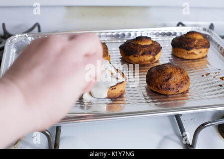Icing freshly baked cinnamon rolls on a cooking pan Stock Photo