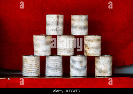 Pyramid of white metal empty soup cans used as targets in a park attraction to entertain pleasurers. A small fly insect sits on one of a can. Red velv Stock Photo