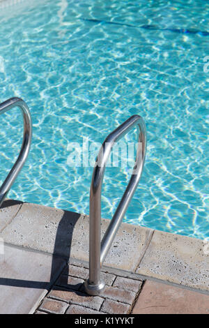 Sunlight glistening off the crystal clear water of a beautiful swimming pool.A view of pool steps enticing the viewer into the cool water on a hot day Stock Photo