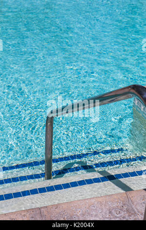 Sunlight glistening off the crystal clear water of a beautiful swimming pool.A view of pool steps enticing the viewer into the cool water on a hot day Stock Photo