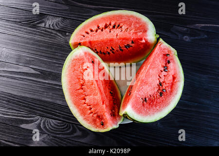 Background of three slices of a cut watermelon in a white plate on a black wooden table top view. Stock Photo