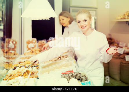 Smiling blonde woman offering fresh and tasty pastry in bakery Stock Photo