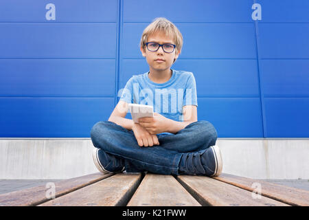 Boy with glasses using mobile phone outdoors Stock Photo