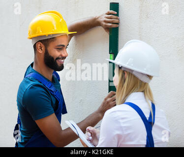 Blonde female engineer and black specialist checking wall plane Stock Photo
