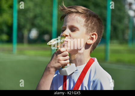 Winner boy football player kisses cup on the football field Stock Photo