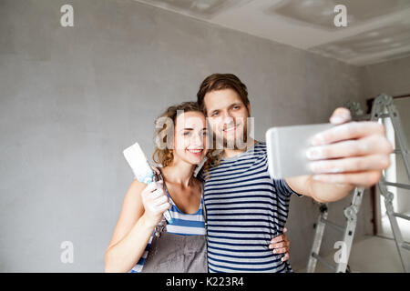 Couple at home painting walls, taking selfie with smartphone. Stock Photo