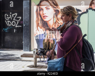 Woman using smartphone with young woman in background, in city street, Liverpool, England, UK Stock Photo
