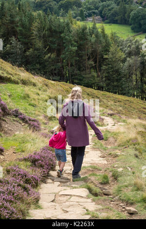 Mature woman helping a young girl down a steep hillside above Edale in the Peak District national park, Derbyshire, England. Stock Photo