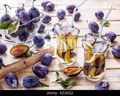 Refreshing drink from fresh juicy sweet sips with lemon in glass mugs with ice cubes on a wooden background with plums and green leaves with plums in  Stock Photo